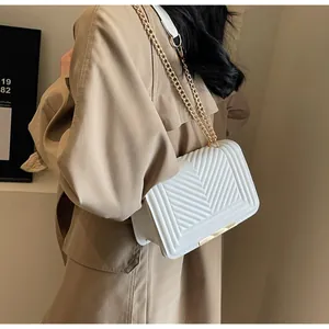 Detail of white quilted chevron shoulder bag with gold chain strap on a khaki trench coat