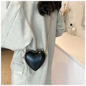 Détail du sac à main cœur noir avec bandoulière chaîne dorée porté sur un blazer