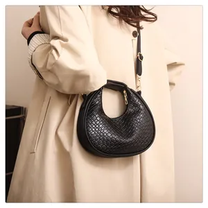 Détail du sac demi-lune noir en cuir tressé avec boucles dorées porté sur un trench