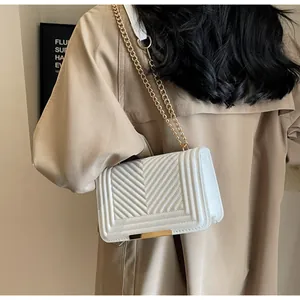 Close-up of a white quilted crossbody bag with golden chain and V-shaped stitching detail