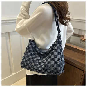 Detail of blue and beige checkerboard denim tote bag with frayed edges worn on shoulder