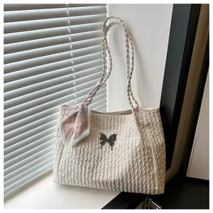 Detail of cream tote bag with wave texture, metal butterfly, and woven strap