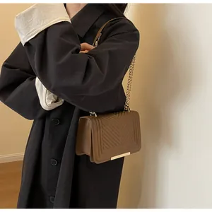 Detail of tan V-quilted shoulder bag with gold chain strap worn on a black wool coat