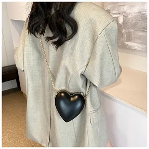 Détail d'un sac à main noir en forme de cœur avec chaîne dorée porté par un mannequin