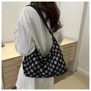 Detail of checkered tote bag with fringe edges and wide black shoulder strap on model