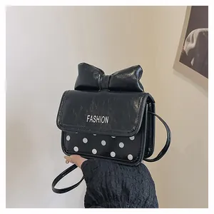 Détail d'un mini sac bandoulière noir avec un grand nœud et un motif à pois blancs