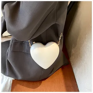 Détail du sac à main blanc en forme de cœur avec chaîne dorée sur un blazer gris