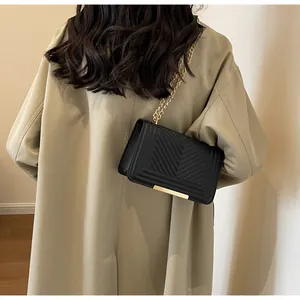 Detail of black chevron quilted shoulder bag with gold chain strap on a model