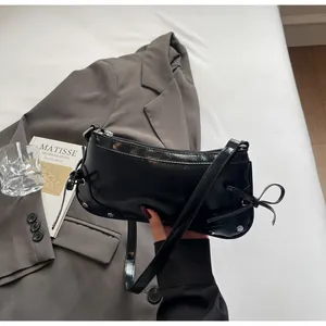 Close-up of black glossy patent leather shoulder bag with metallic rivets and bow detail