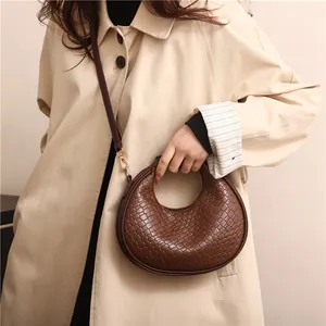 Sac hobo croissant en cuir tressé marron avec bandoulière amovible porté par un mannequin