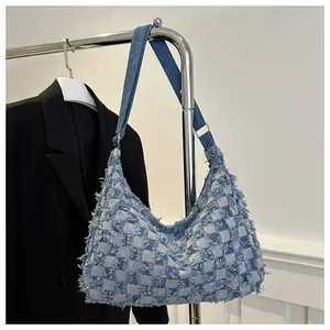 Detail of blue denim checkered tote bag with frayed edges and adjustable metal buckle