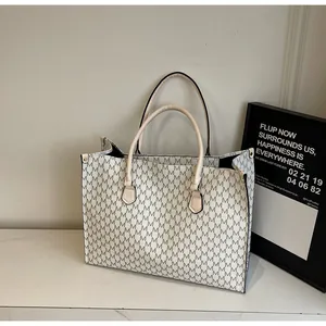 Dettaglio macro della borsa tote in pelle color crema con stampa di lettere e doppi manici