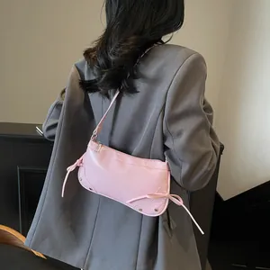 Pink glossy faux leather shoulder bag with rivets and ribbon detail worn by model