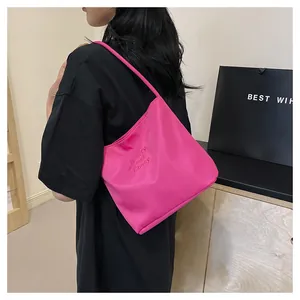 Detail view of pink nylon tote bag with embroidery shown on model's shoulder