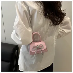 Detail van een roze mini-handtas met een grote strass-strik en een zilveren ketting