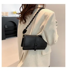 Detail of a black PU leather shoulder bag with unique woven strap worn with a beige blazer