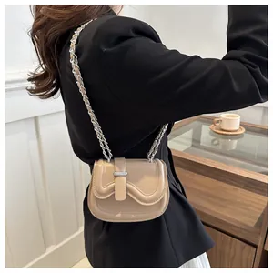 Close-up of khaki leather saddle bag with wavy flap and silver chain on model