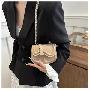 Detail of a beige leather saddle bag with silver chain strap on a stylish outfit