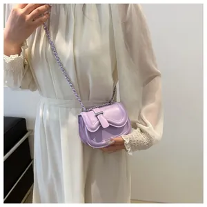 Model wearing a small light purple leather saddle bag with woven chain strap and flap cover