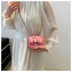 Close-up of a pink mini crossbody saddle bag with a silver chain on a white dress