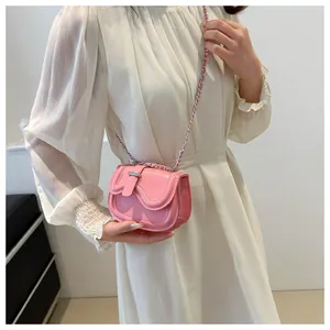 Pink glossy leather saddle bag with wavy stitching and silver chain worn on a white dress