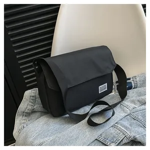 Detail of black canvas messenger bag featuring a woven label on a blue denim background