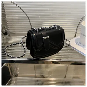 Detail of black leather saddle bag with silver metal clasp and chain strap on a table