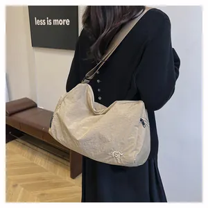 Détail d'un sac bandoulière plissé beige avec large sangle et logo en métal argenté
