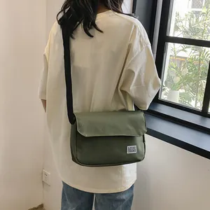 Minimalist dark green canvas messenger bag with adjustable strap worn by a person outdoors