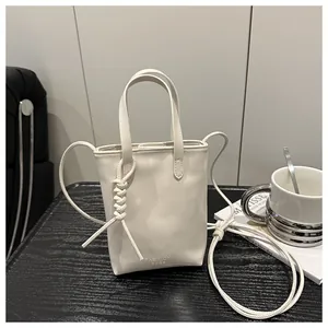 Detail der cremeweißen Mini-Tasche mit Fashion Bags Prägung auf schwarzem Holztisch