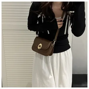 Detail of a dark brown saddle bag with gold horseshoe buckle worn by a model