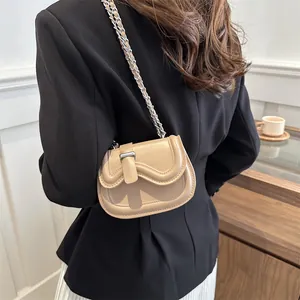 Minimalist beige saddle bag with silver chain strap worn by model in a modern interior