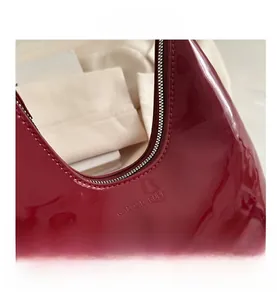 Détail du sac hobo en cuir verni bordeaux avec fermeture éclair et logo gaufré