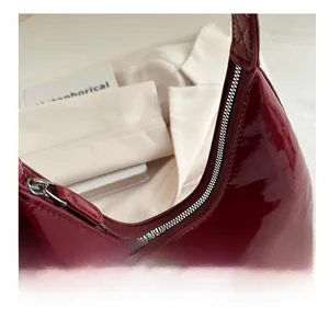 Gros plan du sac hobo en cuir verni bordeaux brillant avec fermeture éclair argentée