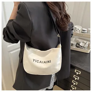 Détail d'un sac demi-lune en toile blanche avec texte YICAIAINI noir et sangle