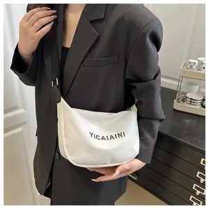 Détail d'un sac bandoulière en toile blanche avec sangle noire réglable et logo
