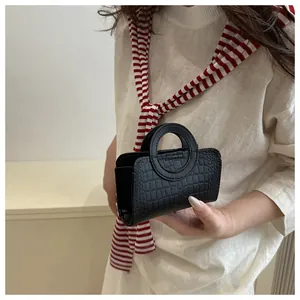 Détail d'un mini sac à main noir à motif crocodile avec poignée ronde porté par un mannequin