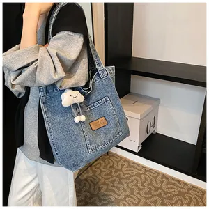 Detail of blue denim tote bag featuring front pocket and white cloud plush charm