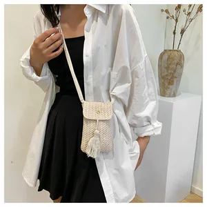 Détail d'un mini sac à bandoulière tissé beige avec pompon décoratif et boucle dorée