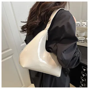 Gros plan du sac bandoulière en cuir verni crème avec finition brillante et logo gravé