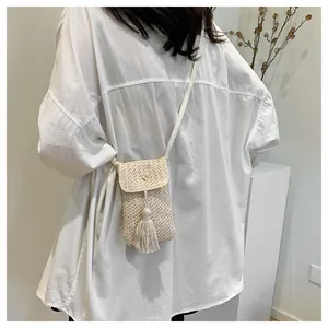 Détail d'un petit sac bandoulière en paille tressée beige avec pompon et fermoir pression
