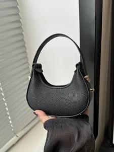 Detail of lychee textured leather and gold buckle on a black crescent mini handbag