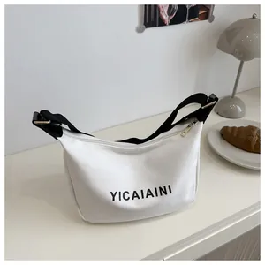 Détail du sac demi-lune en toile blanche avec bandoulière noire et boucles dorées