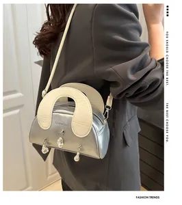 Detail van de zilveren metalen handtas met breed wit handvat en parelhanger aan de onderkant
