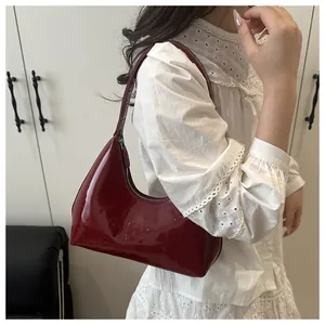 Détail du sac à bandoulière en cuir verni rouge vin brillant porté à l'épaule