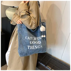 Blue denim tote bag with text print and plush cloud charm on a casual beige trench coat