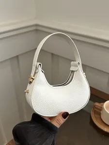 Detail of white lychee leather texture on a crescent handbag with golden metal hardware