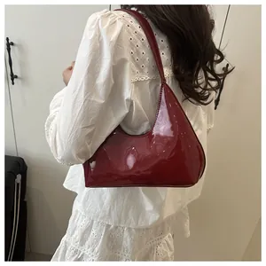 Détail du sac hobo en cuir verni bordeaux à l'épaule avec une tenue en dentelle
