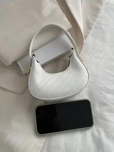 Macro shot of white lychee leather texture on a mini crescent hobo bag with gold hardware
