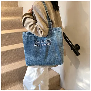 Detail of blue denim tote bag with white 'Less Mondays More Sundays' embroidery